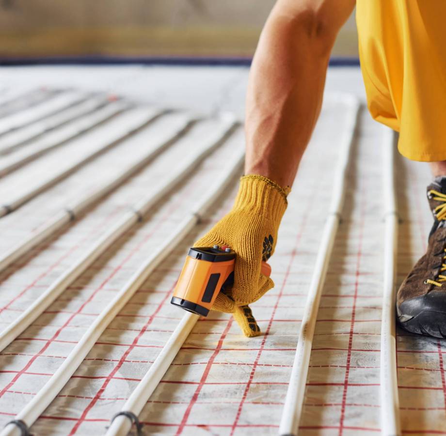 Measures heat of the pipes. Worker in yellow colored uniform installing underfloor heating system.