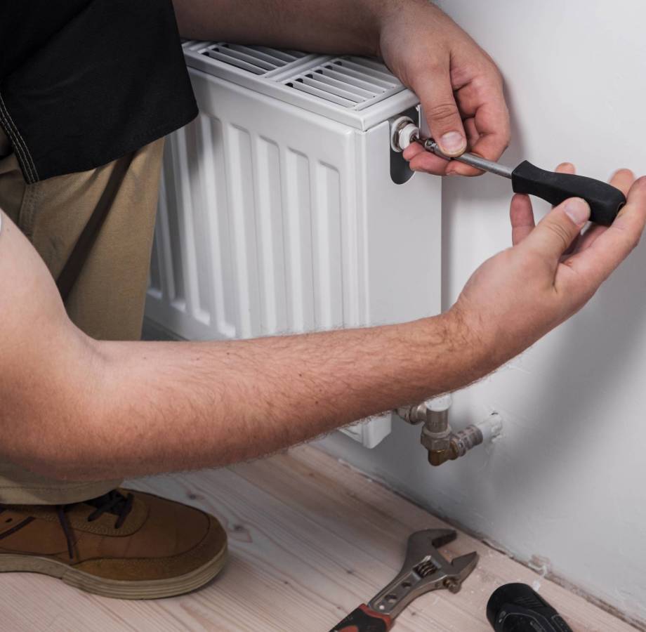 Plumber installing new steel hot water central heating radiator at home